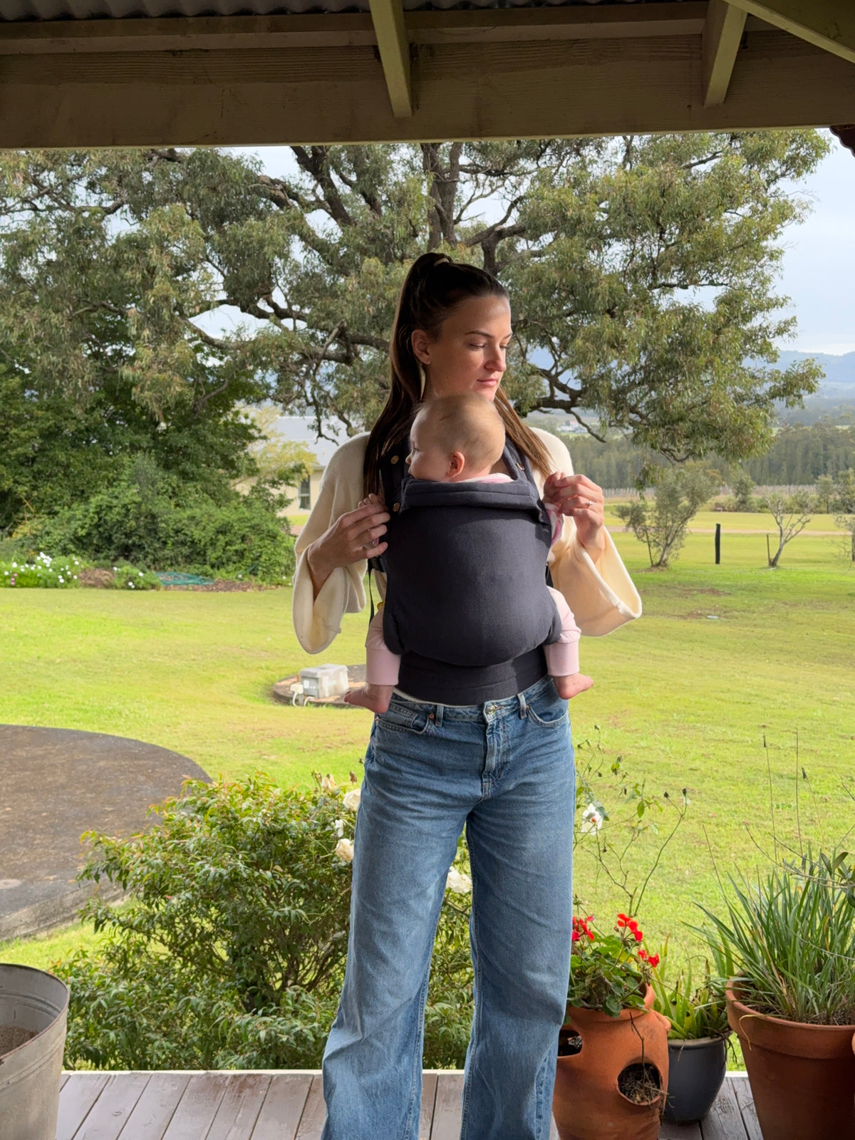Coast | Mum carrying baby in August baby carrier outside with flowers and tree's