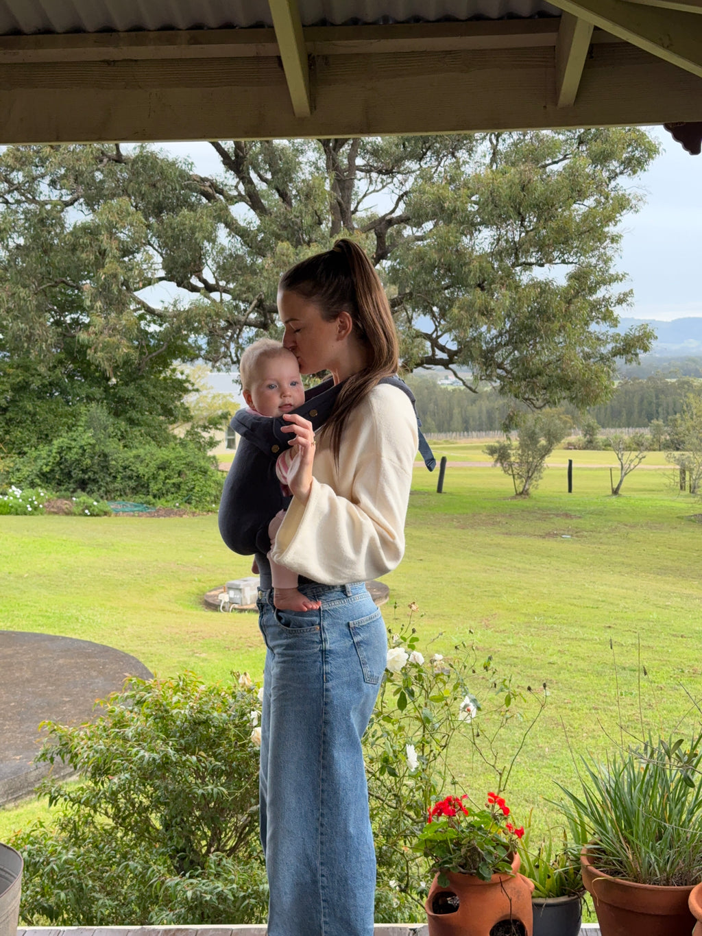 Coast | Mum carrying baby in August baby carrier outside with flowers and tree's side view