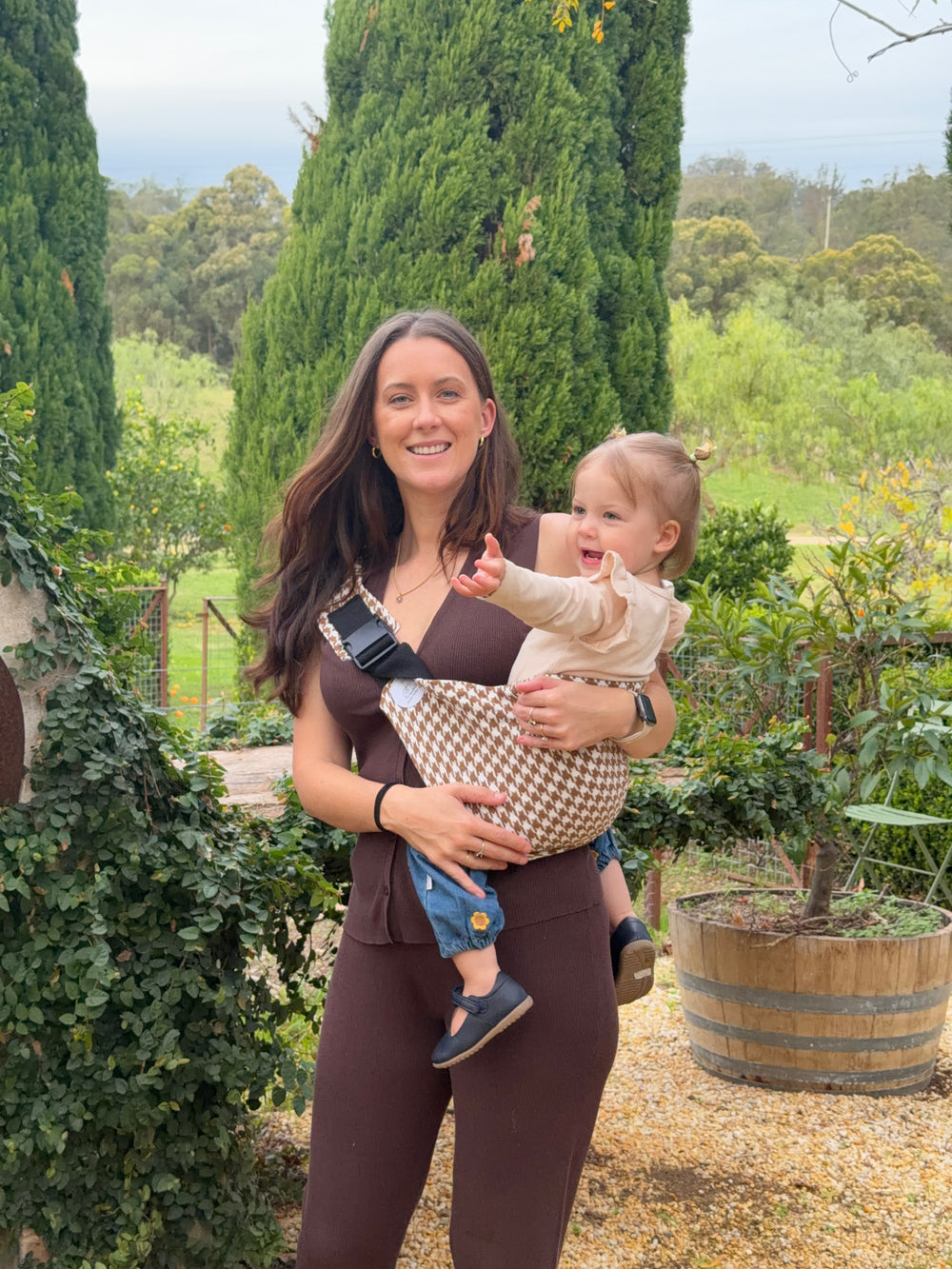 Dune | Woman holding a baby in a Ever carrier outdoors with greenery in the background